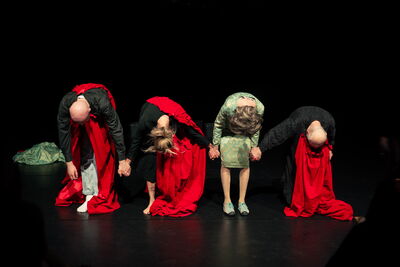 Vier Personen in roten und grünen Gewändern stehen auf einer Bühne. Sie verbeugen sich tief.